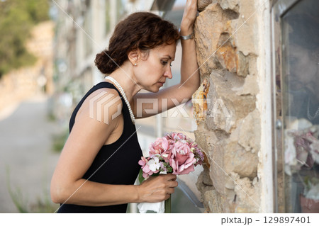 Woman brought flowers to the cemetery and cries over the death of beloved relative Woman brought flowers to the cemetery and cries over the death of beloved relative 129897401