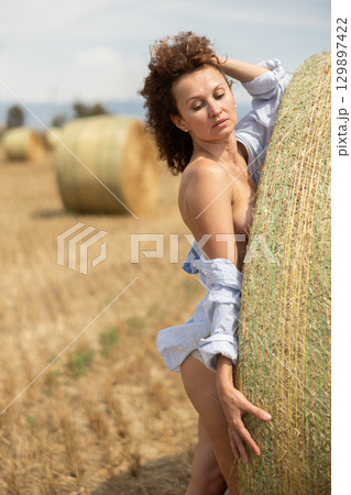Seductive woman in open shirt and lace underwear leaning against hay bale 129897422