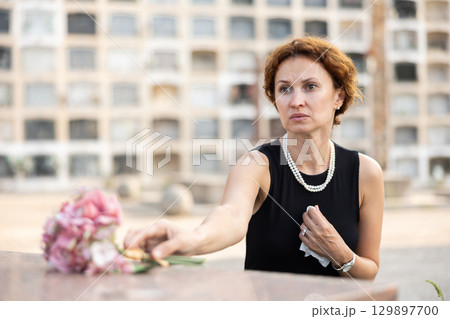 Woman in black laying bouquet on grave in cemetery 129897700