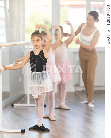 Girls in ballet class perform fifth position with correction of female mentor 129897753