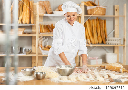 Female employee cooks croissants, rolls dough into tube, forms muffin from raw dough material 129897812