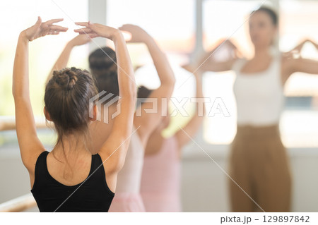 Girls in ballet class perform fifth position with correction of female mentor 129897842