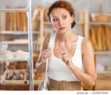 Young European woman near window of bakery food court store examines assortment Young European woman near window of bakery food court store examines assortment 129897844