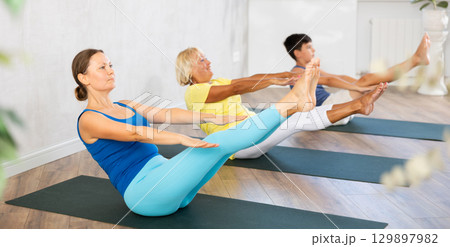 Middle-aged woman practicing boat pose of yoga in light fitness room 129897982