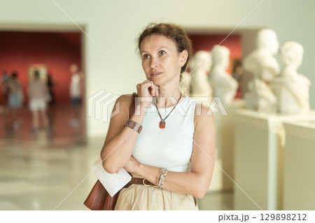 Woman looks at museum sculptures with brochure Woman looks at museum sculptures with brochure 129898212