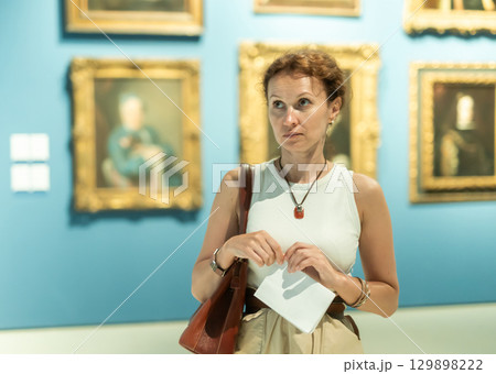 Interested woman in casual clothes exploring paintings in halls of museum Interested woman in casual clothes exploring paintings in halls of museum 129898222