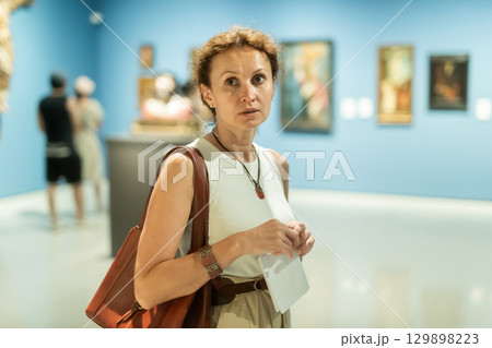 Portrait of beautiful woman looking at pictures and amaze in museum, holding guide book Portrait of beautiful woman looking at pictures and amaze in museum, holding guide book 129898223