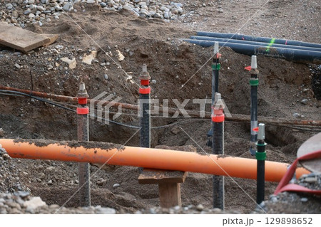 Bunch of pipes are in the dirt, with some of them being orange Bunch of pipes are in the dirt, with some of them being orange 129898652