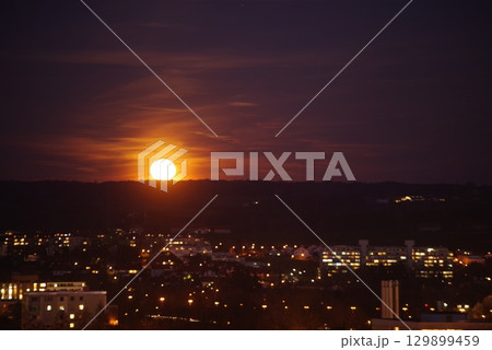 The sun is setting over a city, with the sky turning dark 129899459