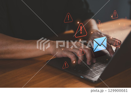 Person types on a laptop computer while warning email icons appear, symbolizing threats like phishing, malware, data breaches, scam messages, spam risks, and the need for cybersecurity protection. 129900081