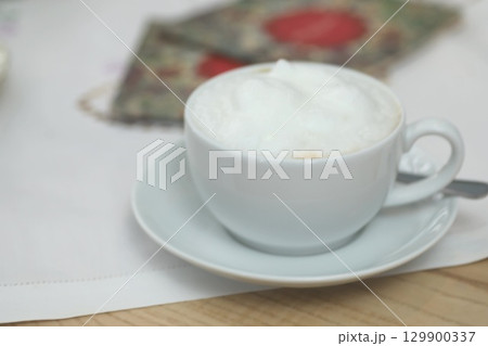 White coffee cup with foam on top sits on a white saucer 129900337