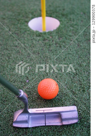 Golf ball is sitting on a green field next to a golf club Golf ball is sitting on a green field next to a golf club 129900378
