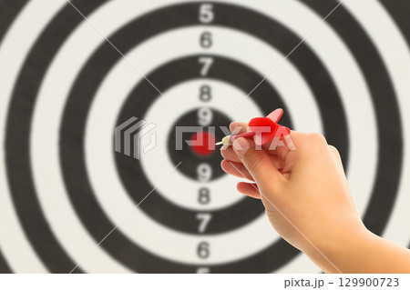 A hand releases a red dart aimed at a bullseye target on a wall A hand releases a red dart aimed at a bullseye target on a wall 129900723
