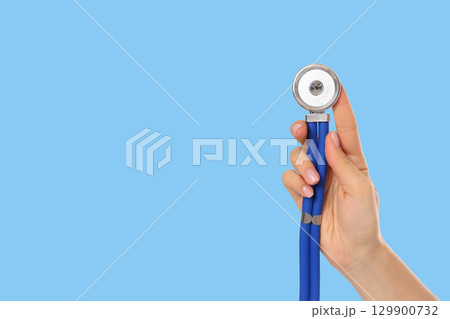 Stethoscope is held in a hand against a light blue backdrop 129900732