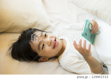 寝転んでスマホを見る子供 129901533