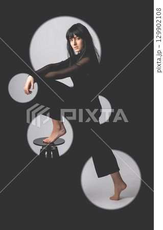 Woman portrait with dark hairs and clothes with one leg on chair 129902108