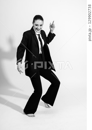 Woman wearing classic black suit and dancing on studio white background Woman wearing classic black suit and dancing on studio white background 129902738