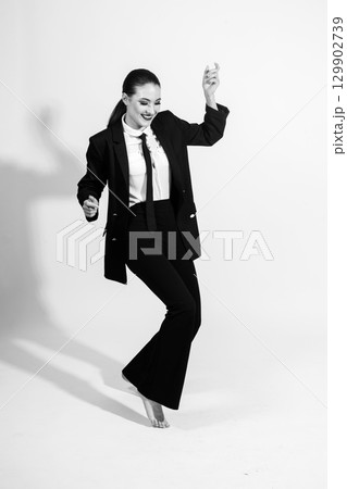 Woman wearing classic black suit and dancing on studio white background Woman wearing classic black suit and dancing on studio white background 129902739