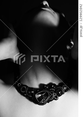 Part of woman face silhouette with black necklace hiding in shade 129902842