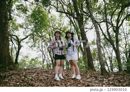 Two female friends with backpacks on vacation hiking through countryside together. Asian friend girls backpacker friend travel in forest wild together. happy and enjoying sunny day while hiking. Two female friends with backpacks on vacation hiking through countryside together. Asian friend girls backpacker friend travel in forest wild together. happy and enjoying sunny day while hiking. 129903010