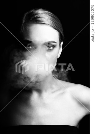 Studio portrait of beautiful woman blowing smoke from mouth Studio portrait of beautiful woman blowing smoke from mouth 129903079