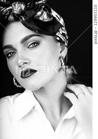 Studio portrait of beautiful woman with scarf on her head touching her neck with hand 129903110
