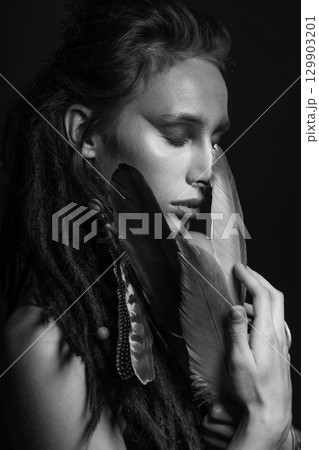 Studio portrait of woman with make-up, dreadlocks and bird feathers 129903201