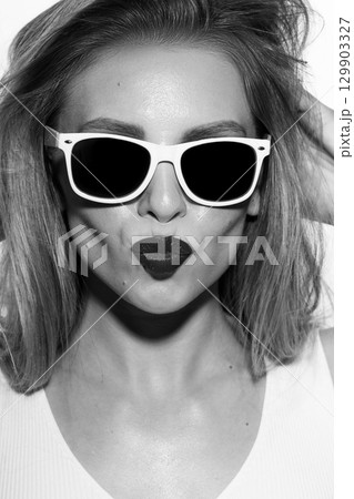 Beautiful woman close-up studio portrait with white sunglasses sending kiss 129903327