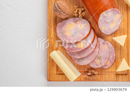 Sliced sausage with cheese cubes and walnuts on wooden board served with cheese pieces. top view. copy space Sliced sausage with cheese cubes and walnuts on wooden board served with cheese pieces. top view. copy space 129903679