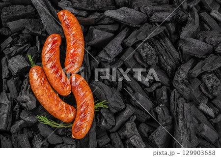 Grilled sausages on charcoal background with rosemary garnish. top view. copy space 129903688