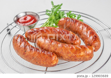 Grilled sausages with ketchup and parsley served on metal rack over white background 129903689