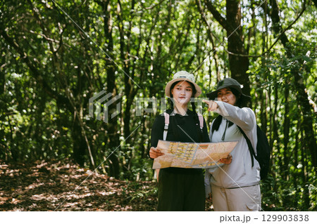 Two female friends with backpacks on vacation hiking through countryside together. Asian friend girls backpacker friend travel in forest wild together. happy and enjoying sunny day while hiking. 129903838