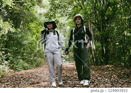 Two female friends with backpacks on vacation hiking through countryside together. Asian friend girls backpacker friend travel in forest wild together. happy and enjoying sunny day while hiking. 129903932
