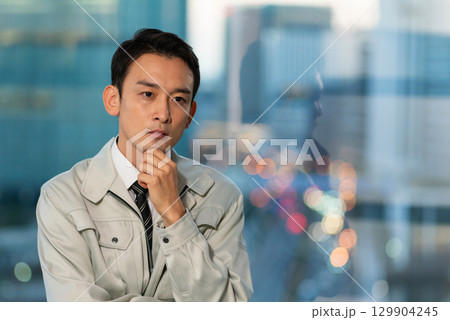 高層ビルをバックに腕組みをして考える作業着の男性 高層ビルをバックに腕組みをして考える作業着の男性 129904245