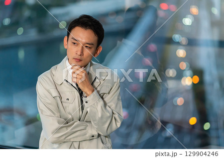 高層ビルをバックに腕組みをして考える作業着の男性 高層ビルをバックに腕組みをして考える作業着の男性 129904246