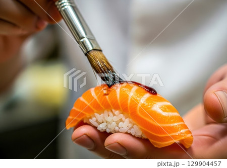 新鮮なサーモン握りにタレを塗る寿司職人の手元 129904457