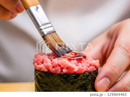 ネギトロ軍艦に醤油を塗る寿司職人の手元写真 129904465
