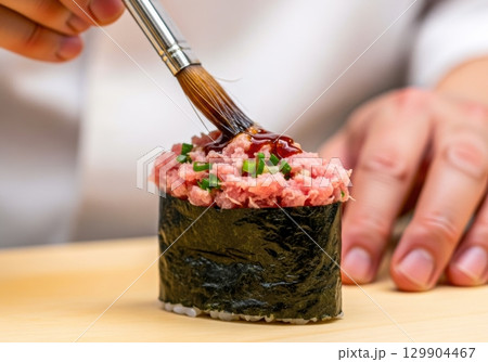 ネギトロ軍艦に醤油を塗る寿司職人の手元写真 129904467
