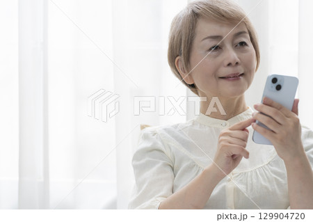 寝室のベッドでスマホを操作するシニア女性 129904720