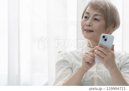 寝室のベッドでスマホを操作するシニア女性 129904721