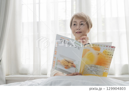 寝室のベッドで雑誌を見るシニア女性 寝室のベッドで雑誌を見るシニア女性 129904803