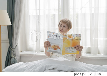 寝室のベッドで雑誌を見るシニア女性 寝室のベッドで雑誌を見るシニア女性 129904805