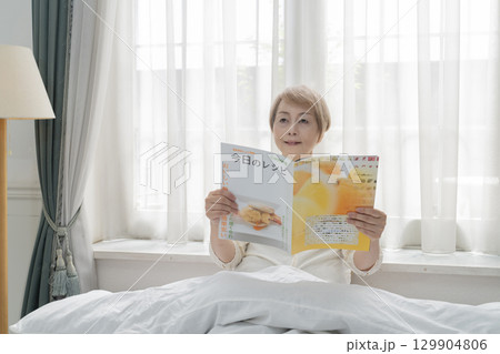 寝室のベッドで雑誌を見るシニア女性 寝室のベッドで雑誌を見るシニア女性 129904806