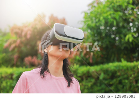 Young woman wearing virtual reality headset outdoors, female exploring VR technology in nature, person experiencing immersive digital world with modern gadget and innovation. Young woman wearing virtual reality headset outdoors, female exploring VR technology in nature, person experiencing immersive digital world with modern gadget and innovation. 129905093