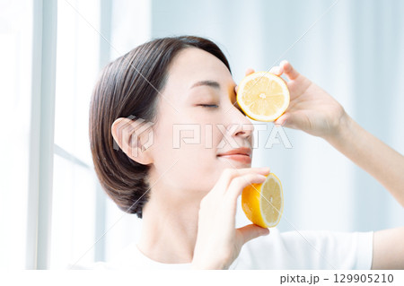 光の中でレモンを両手に持つ透明感のある女性 顔のアップ 光の中でレモンを両手に持つ透明感のある女性 顔のアップ 129905210