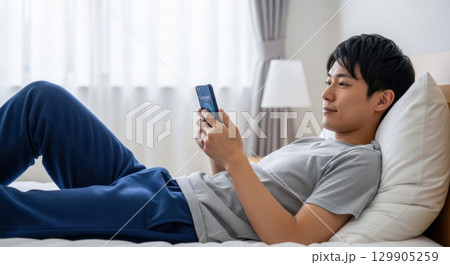 ベッドでスマホを操作するリラックスした男性 129905259