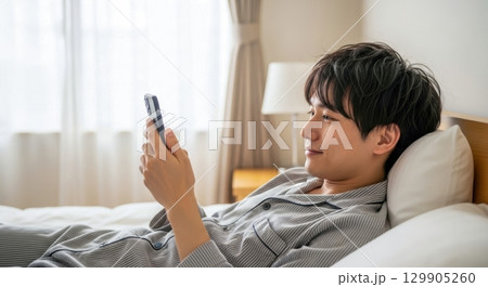 ベッドでスマホを操作するリラックスした男性 129905260