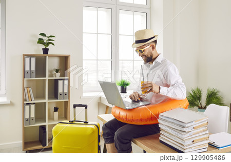 Funny man sitting at the desk of his workplace at office and booking tickets for summer vacation. 129905486