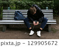 A teenage boy on a bench tying his shoelaces. 129905672