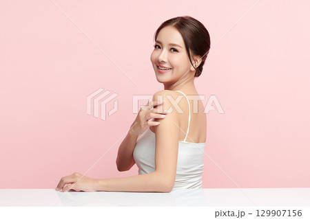 A beautiful young Asian woman with clean, fresh skin against a pink background. Skincare, facial treatment, cosmetology, beauty, and spa. An elegant portrait of an Asian woman. 129907156